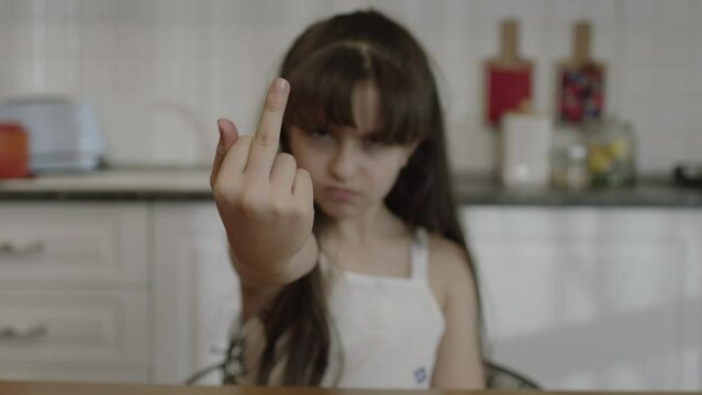 Little girl angry, angry and disobedient at bad behavior showing middle finger. In the kitchen, the middle finger points badly and asks not to be disturbed. Provocation and rude attitude.