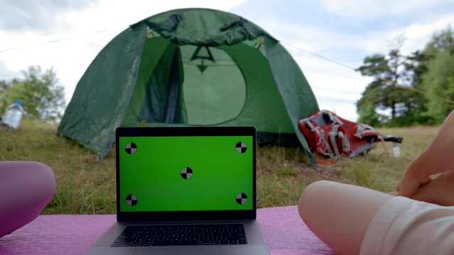 Couple watches laptop with chromakey green screen together on grass against green camp tent. Man and woman enjoy spending time together on vacation in campground closeup