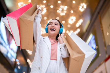 Smiling asian woman hold shopping bags listening music headphone. Young woman relax shopping in shopping mall Purchases, black friday, discounts, sale concept. Online shopping concept.