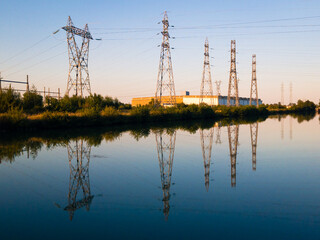 A row of metallic transmission towers of various shapes reflecting in the still water of a canal...