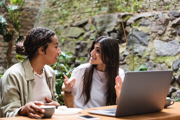 Interracial girlfriends talking near gadgets and coffee in outdoor cafe