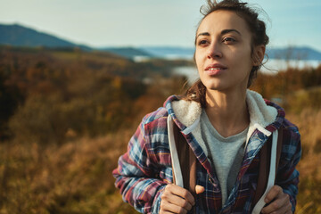 Close up face young confident woman hiker standing on the slope of mountain ridge against mountains, looking away, enjoying the epic view