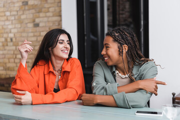 Positive multiethnic girlfriends talking near smartphone in cafe