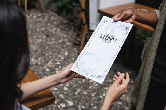African american waitress holding menu near blurred client in outdoor cafe