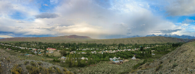 Fototapeta na wymiar 180 degree panorama of the village of Kyzyl Tuu with dramatic sky in Kyrgyzstan.