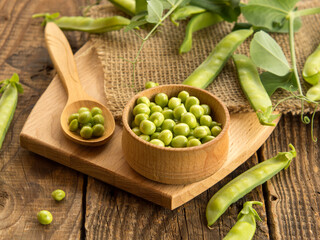 wooden bowl and spoon with fresh peas and their pods on an old wooden table, rustic background with peas