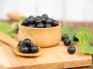 Fresh blackcurrant berries in a bowl on a wooden table near green leaves. Juicy natural currant fruits. Black currant