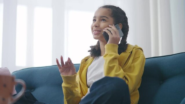 African American teen girl talking on phone on sofa at home, rest time, gadgets