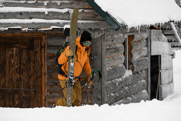 man with backpack and skis and ski poles in his hands against the background of wooden hut.