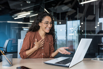 Fototapeta na wymiar Happy hispanic businesswoman working in modern office using laptop for video call and online meeting with fellow employees, woman smiling and having fun giving a presentation