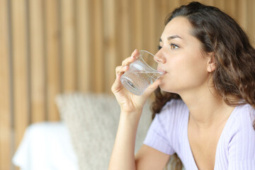 Relaxed woman drinking water in a bedroom