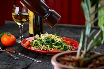 salad with meat, cheese, arugula and tomatoes in a red plate, macro photo sprinkled with pepper

