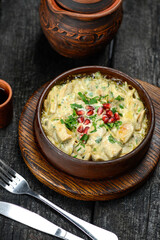 baked meat in a cream sauce in a pan with greens and pomegranate berries vertical photo
