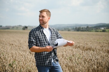 Handsome farmer with tablet standing in front of combine harvester during harvest in field.