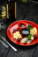 slicing of various cheeses with honey and grape jam in a red plate, vertical photo
