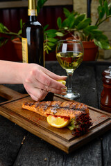 large grilled salmon fillet on wooden board with lemon in female hand
