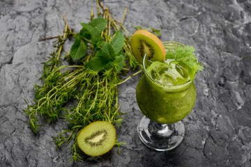 smoothie cocktail with kiwi in a glass on a dark background with greens and kiwi
