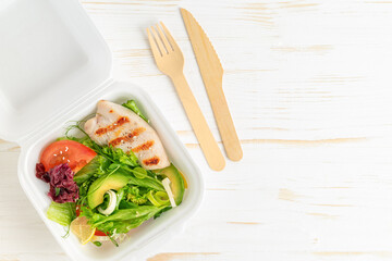 Lunch boxes with salad and grilled chicken on white wooden background. Top view