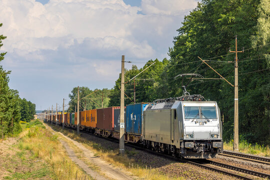 Nowoczesna srebrna lokomotywa elektryczna z pociągiem z kontenerami pokonuje kolejne kilometry linii kolejowej