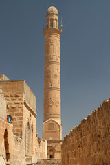 Obraz premium A view of the high ornate minaret of the Mardin Grand Mosque from a narrow street in the historic part of the city of Mardin in the Southeast Anatolia region of Turkey