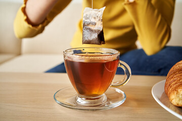 Tea bag above a cup of tea on a table, indoors
