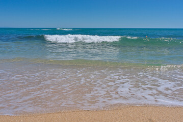 Clear emerald green sea with white foam and clean sandy beach
