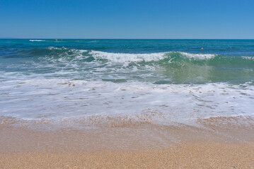 Clear emerald green sea with white foam and clean sandy beach