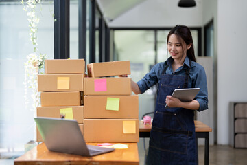 Young attractive asian woman owner startup business with box at home prepare parcel delivery in sme...