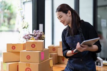Young attractive asian woman owner startup business with box at home prepare parcel delivery in sme...