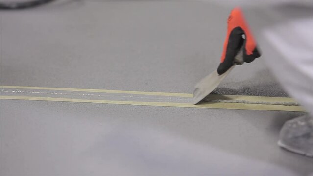 The builder covers the joint seam with sealant. Construction worker grouting seams in concrete floor