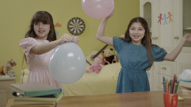 Little girls are blowing air into the balloon. Happy birthday party, celebration. Children are having fun by inflating balloons in their rooms. Cute kids inflate the balloon for their birthday.