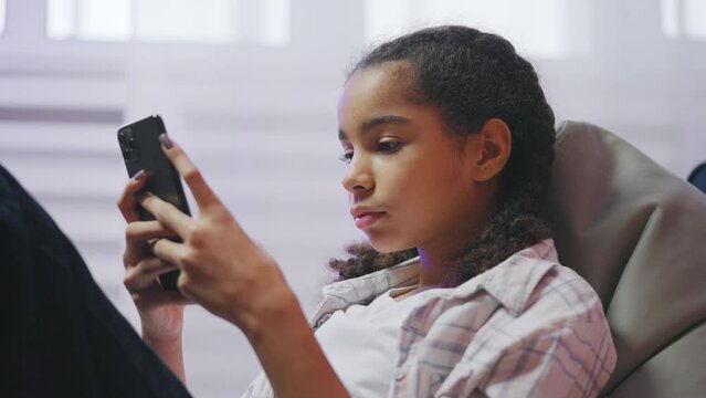 African American teenage girl reading upsetting social media post on smartphone
