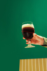 Female hand holding glass of cold dark beer over dark green background. Oktoberfest, vacation,...