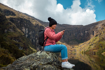 Naklejka premium Excursionista atractivo sentado y sosteniendo un teléfono junto a un lago tranquilo en las hermosas montañas