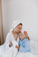 Mom and her little daughter in bathrobes and towels on their heads drink tea in bed. Family concept. 
