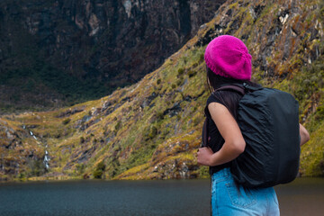 Atractiva excursionista de pie junto a un tranquilo lago en las hermosas montañas.