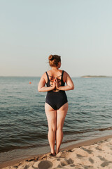 Caucasian woman practicing yoga at seashore sandy beach on sunrise. Womens health and wellness. Sports body positive. Real instructor poses