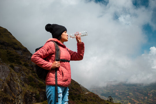Caminante en una chaqueta rosa bebiendo agua contra un cielo azul nublado
