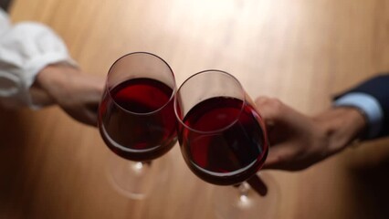 Close-up top view of unrecognizable happy couple clinking wine glasses enjoying nice romantic dinner in modern restaurant. Loving couple celebrating anniversary indoors at home at table.