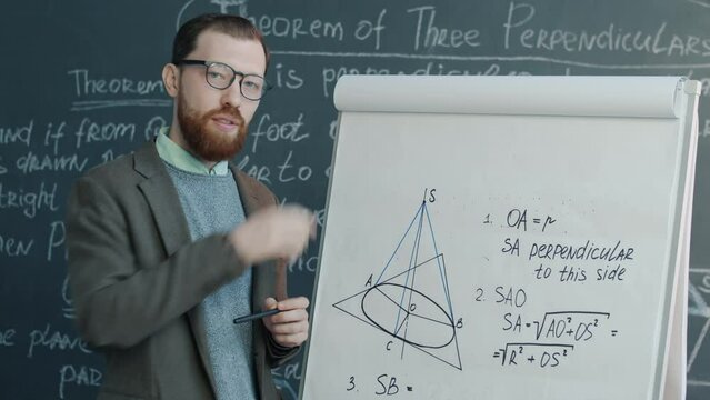 Portrait of college maths teacher pointing at drawings on flipchart speaking and looking at camera teaching online during pandemic. Remote education concept.