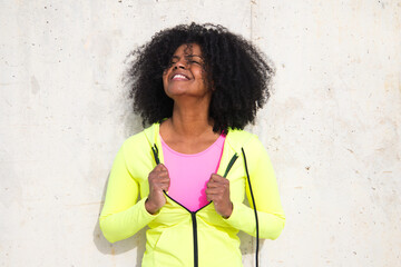 Beautiful young Afro-American woman in bright green and pink sportswear on a grey concrete wall texture background. Woman makes different expressions. Laughing, serious, happy, sad, thinking