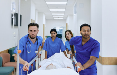Doctors and nurses wheeling elderly patient in gurney on hospital corridor at emergency department. Work of emergency medical team and paramedics