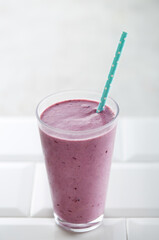 Blueberry smoothie with straw on a white background. Copy space