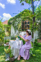 young woman in a princess dress sits at a vintage table with cookies and books in her backyard with...