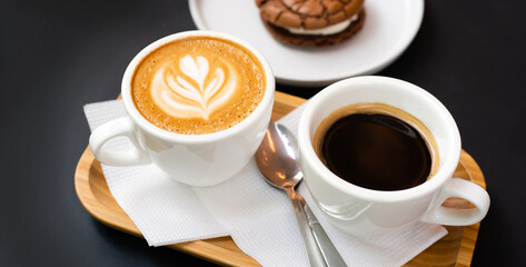 Cup of fresh coffee and cup of cappuccino with chocolate cake on the black table in a street cafe. Banner. Close-up. Selective focus.