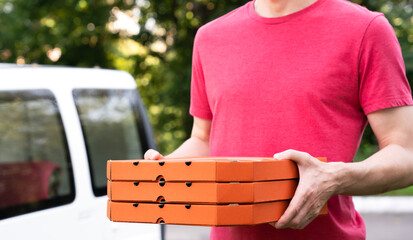 A pizza delivery man holds pizza boxes near the car outdoor. Mockup. Selective focus.