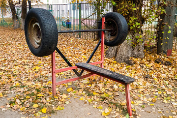Wooden bench and homemade barbell made of wheels are outdoors in the yard