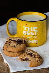Cookies with chocolate pieces, milk in a ceramic mug. On the yellow mug it says The best is yet to come