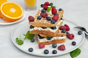 Fresh Viennese or Belgian waffles on a plate with fresh raspberries and blueberries and whipped cream.