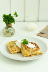Pancakes with filling, sour cream and parsley on a white plate